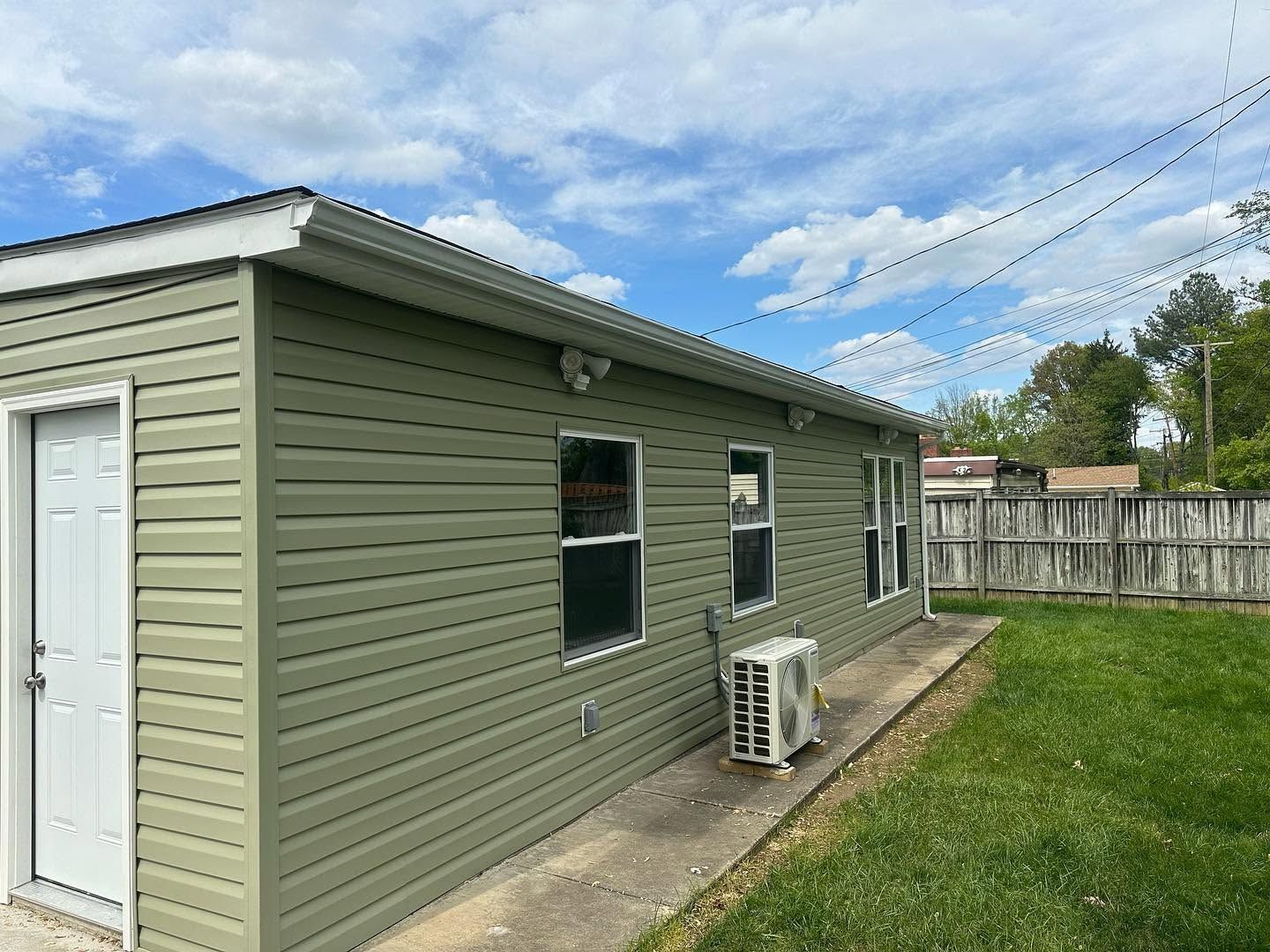 Green-sided garage with white door, window, and air conditioner beside a grassy yard and wooden fence.