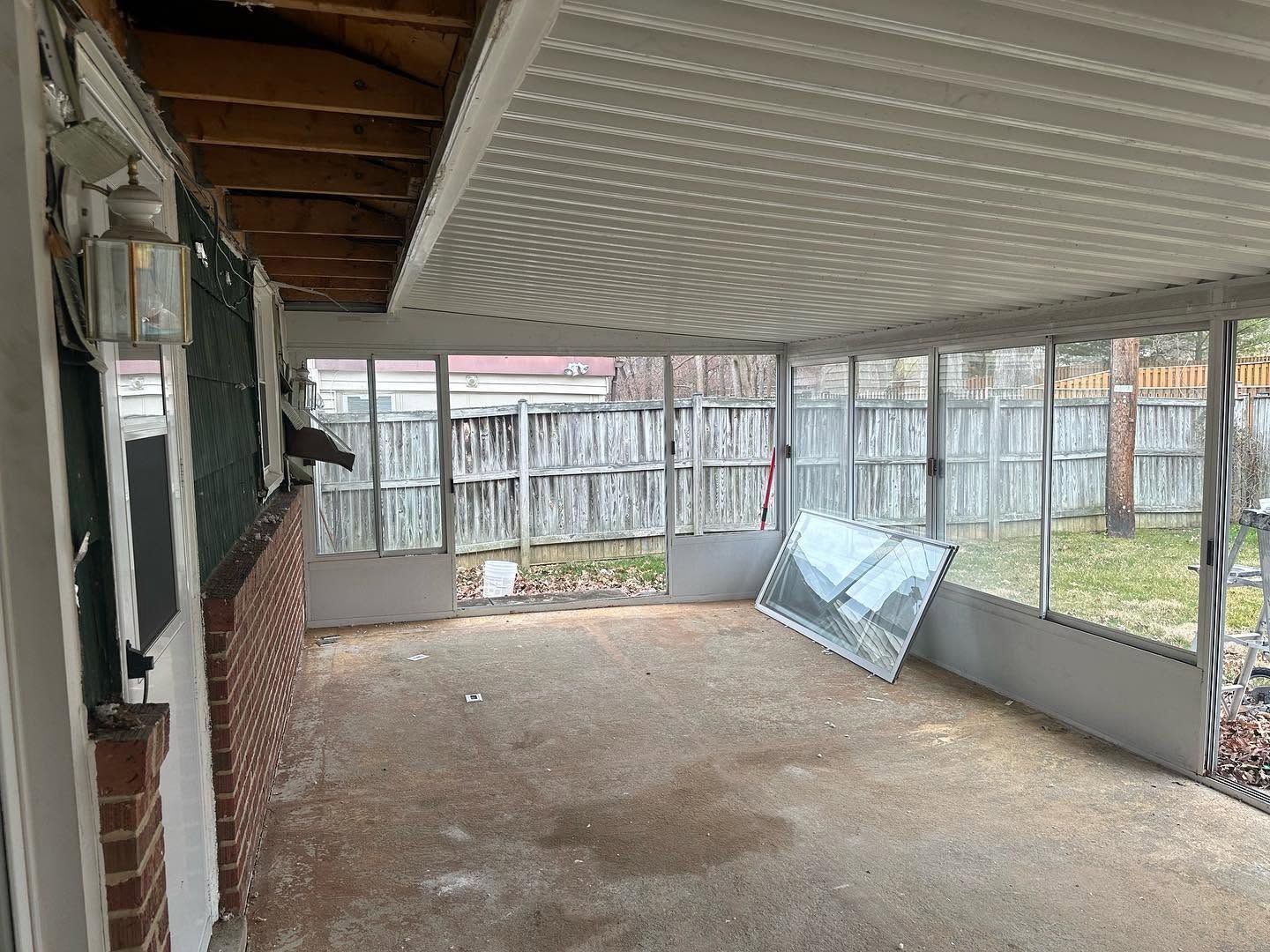 Covered patio with corrugated roof, brick wall, concrete floor, and stacked glass panels by a fenced yard