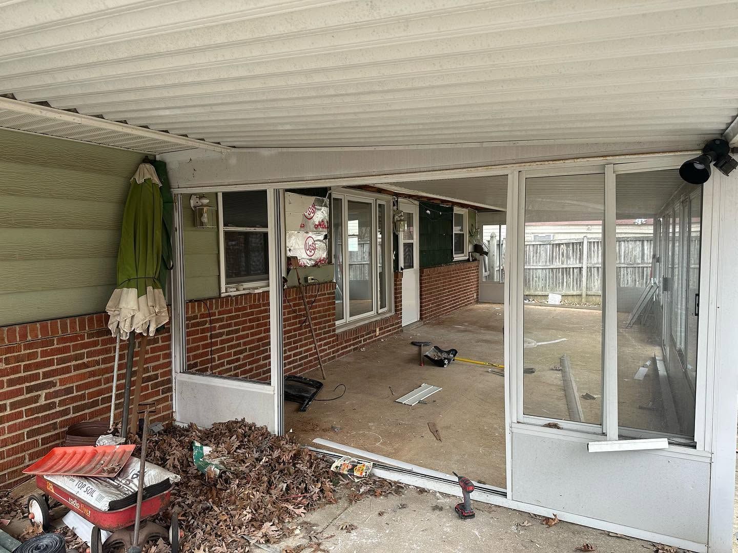 Enclosed brick porch with damaged screens, debris on the floor, and a ceiling fan under a covered roof