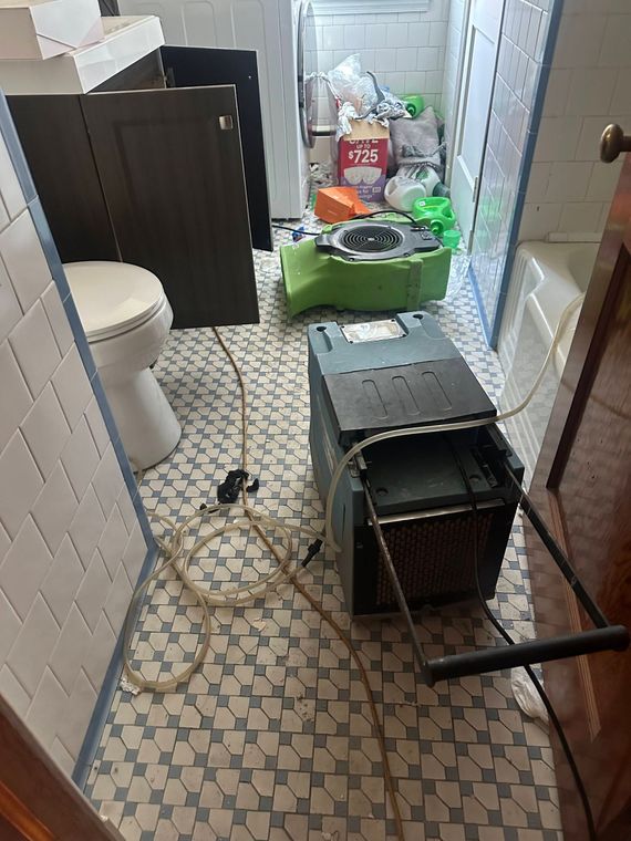 Cluttered narrow hallway with cleaning supplies, a toilet, cords, and a black crate on the floor.
