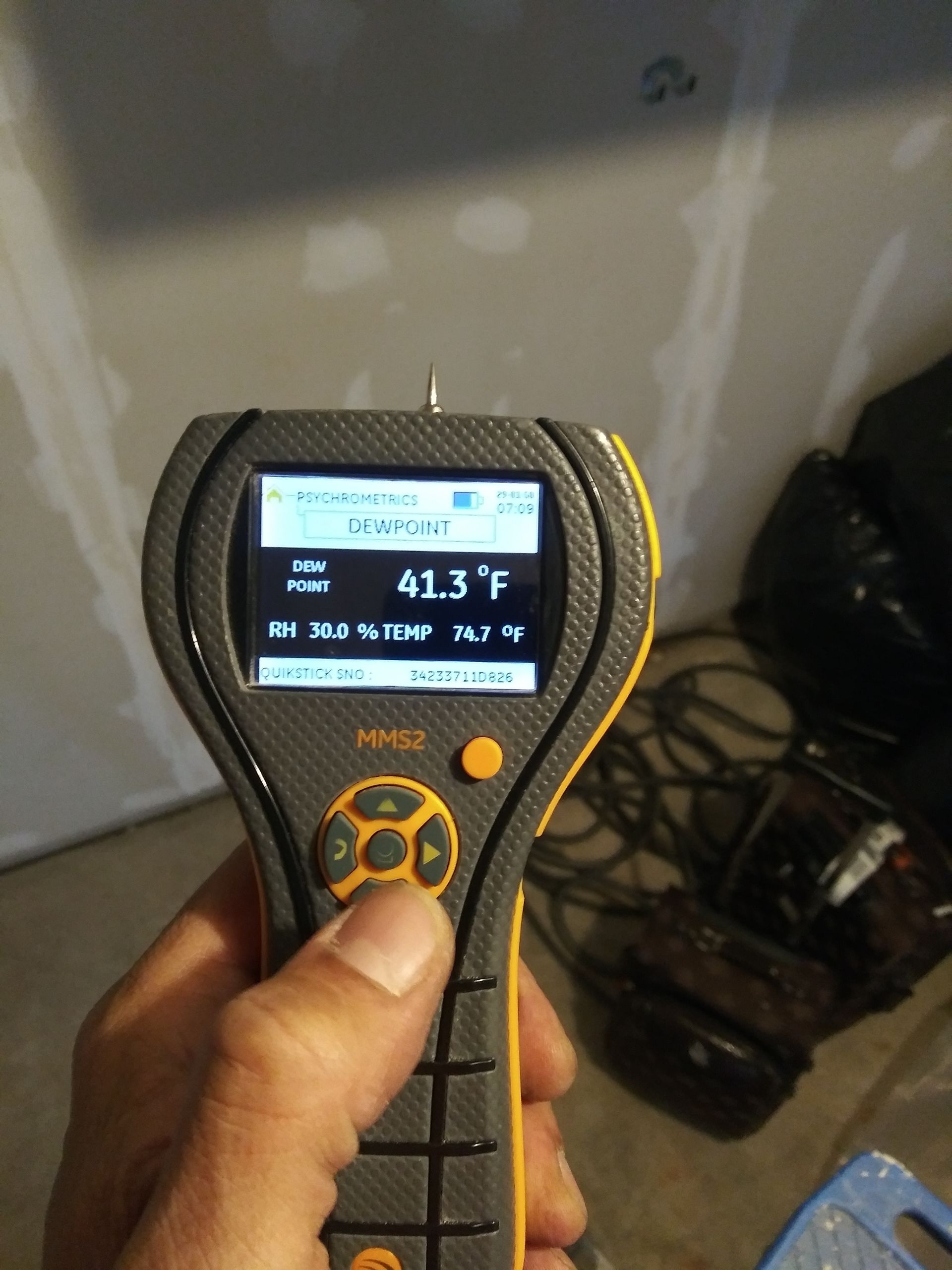 Hand holding a digital infrared thermometer showing 41.3°F against a wall with cables and wires behind it