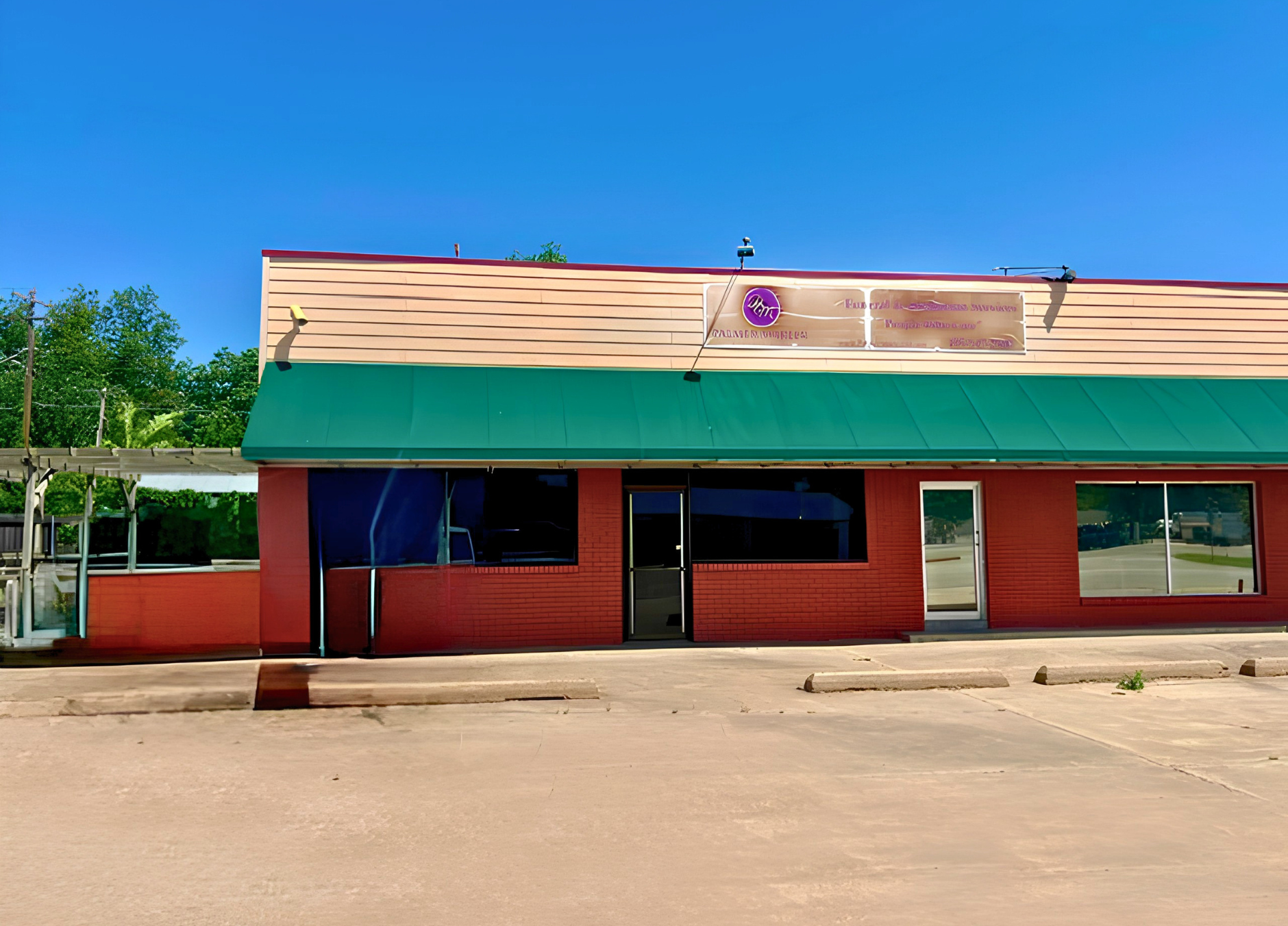 Small storefront with red walls, teal awning, and beige roof under a clear blue sky.