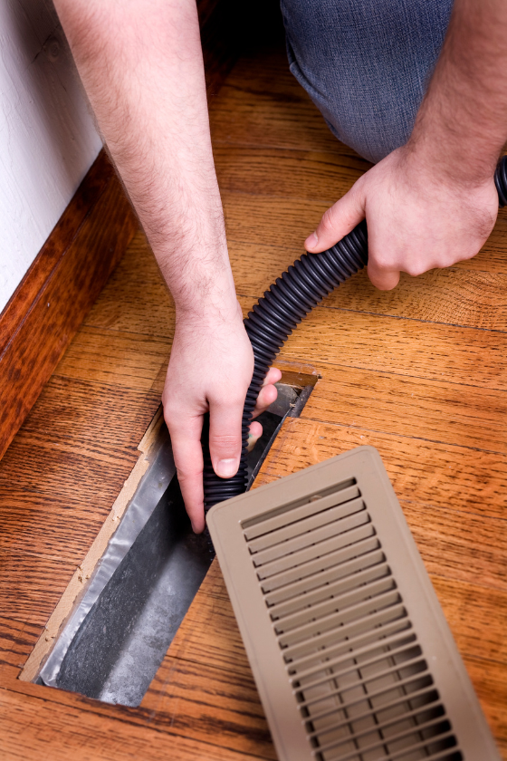 A person is cleaning a vent with a vacuum hose.