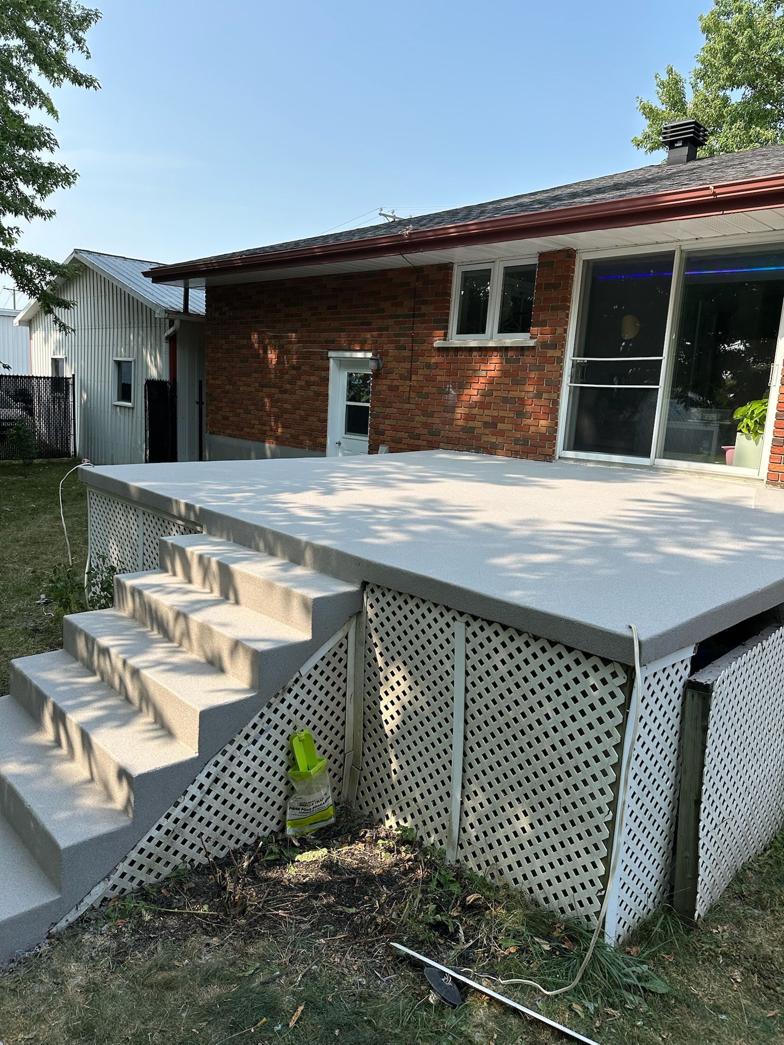 Une terrasse en béton avec des marches et des plinthes en treillis contre une maison avec une porte et des fenêtres