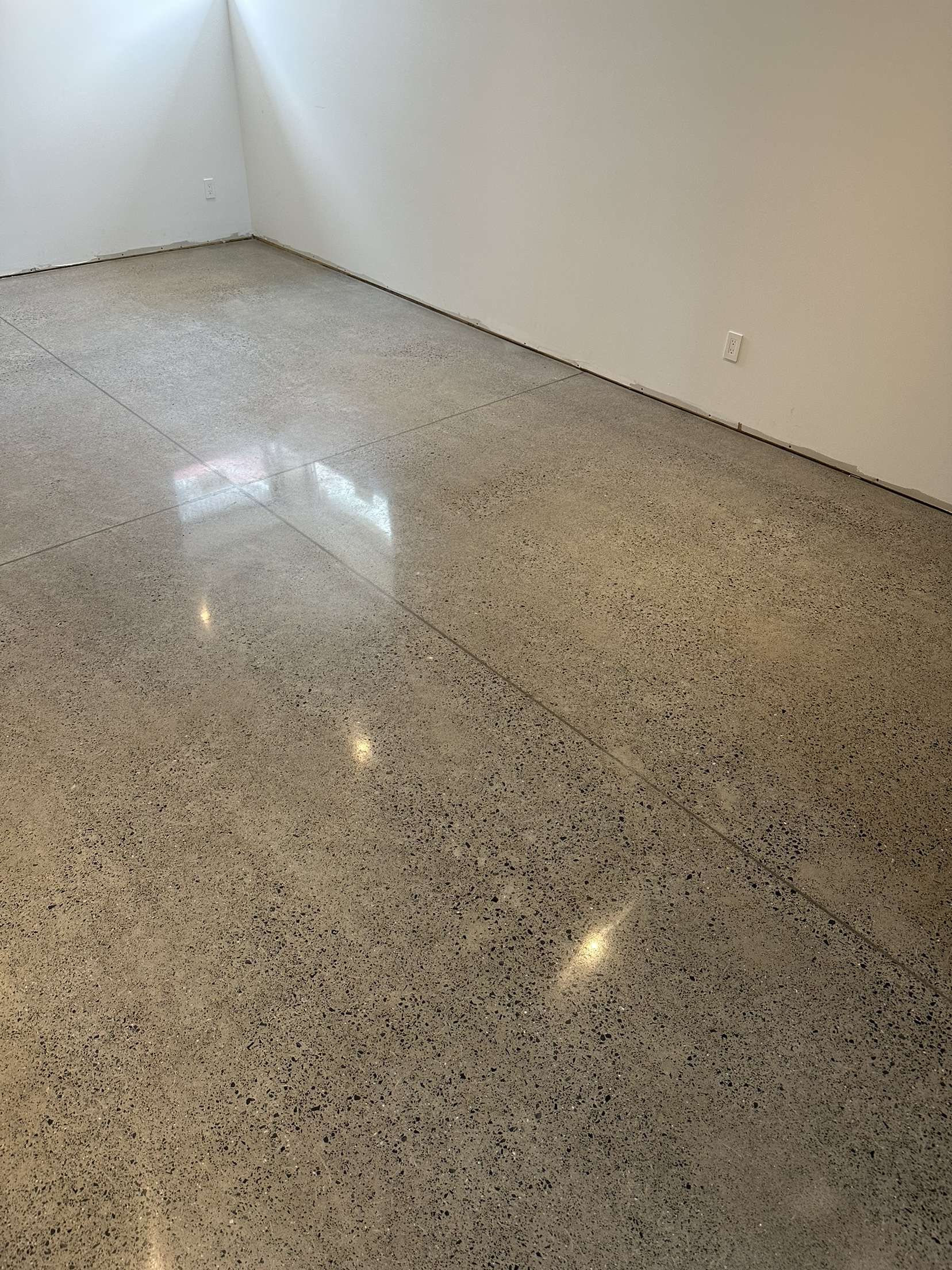 Sol en béton poli dans une pièce aux murs blancs ; lumière se reflétant sur la surface.