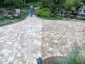 Person walking on a stone patio in a lush garden beside a waterfall and chairs