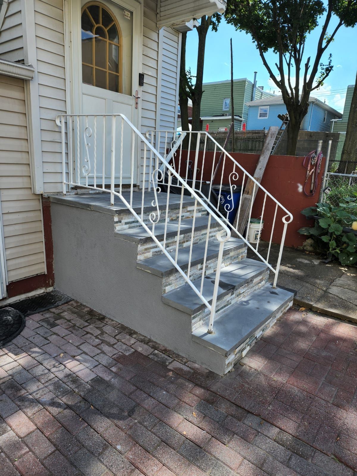 Front steps of a house with a white metal railing and small concrete landing by a brick walkway