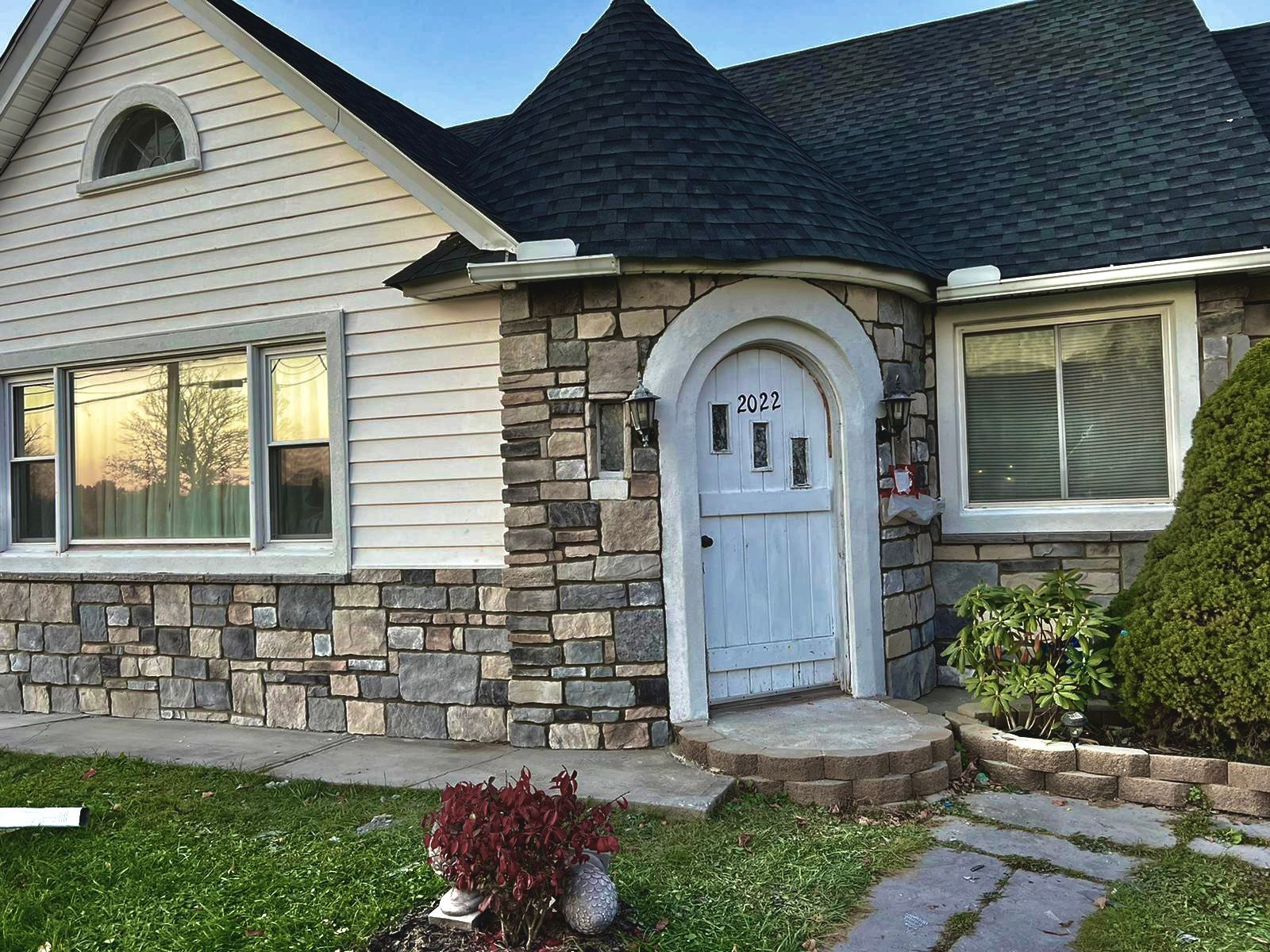 Suburban house exterior with white siding, stone facade, arched front door, and small front garden