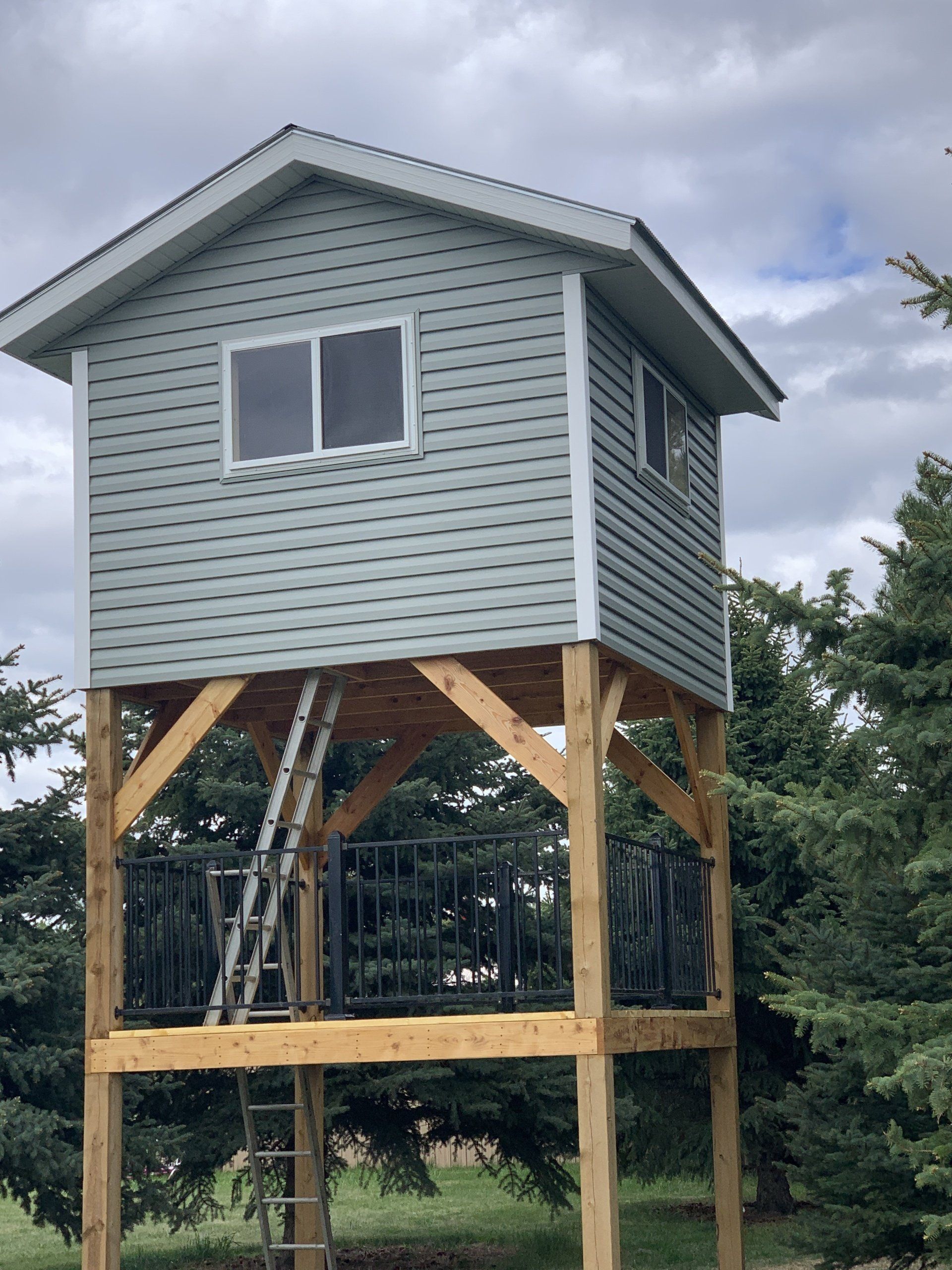 Elevated light blue shed-style treehouse on wooden stilts in a grassy yard