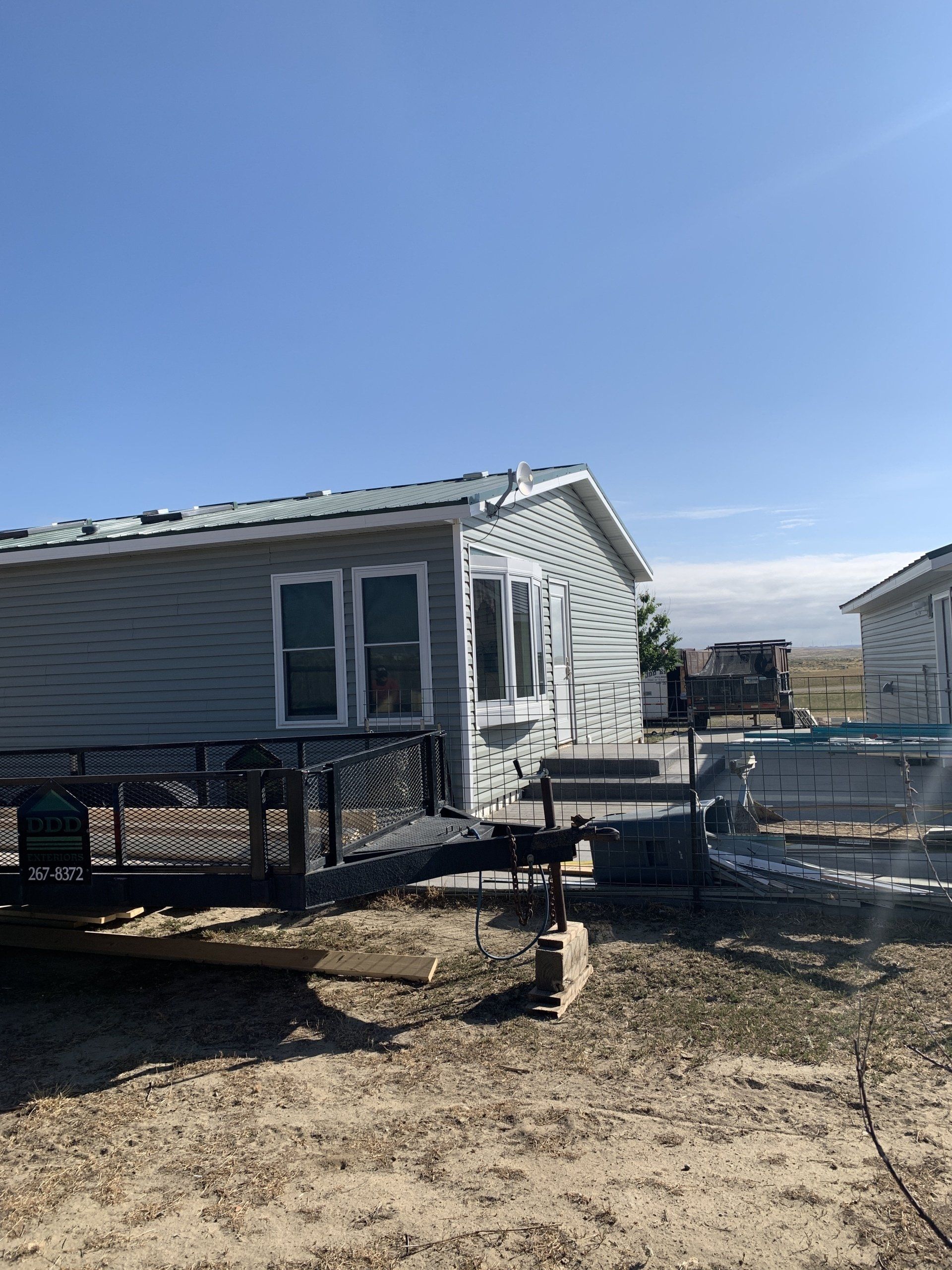 Mobile home on a raised deck in a bare yard under a clear blue sky.