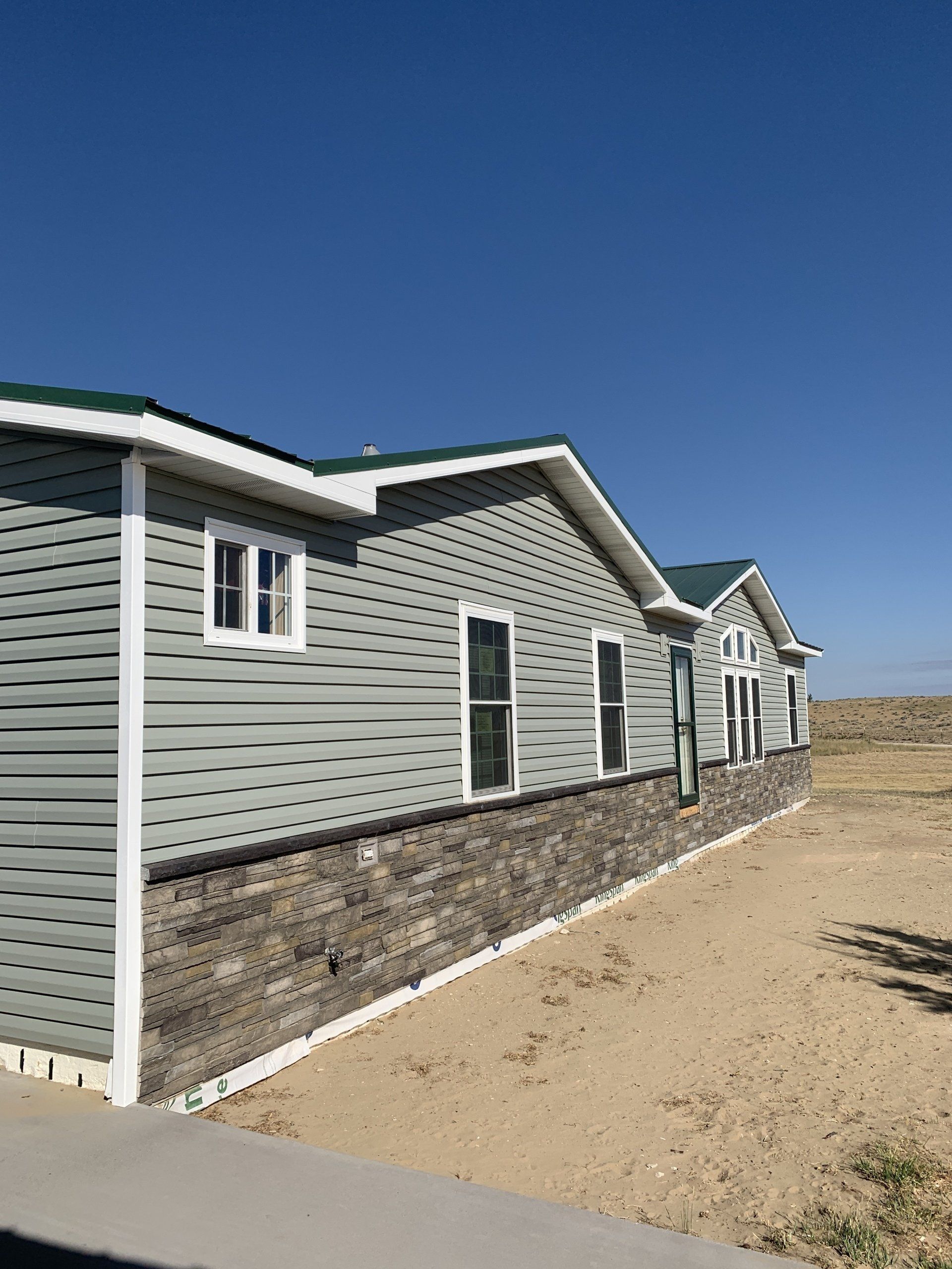 Row of gray-sided homes with stone bases beside a sandy path under a clear blue sky