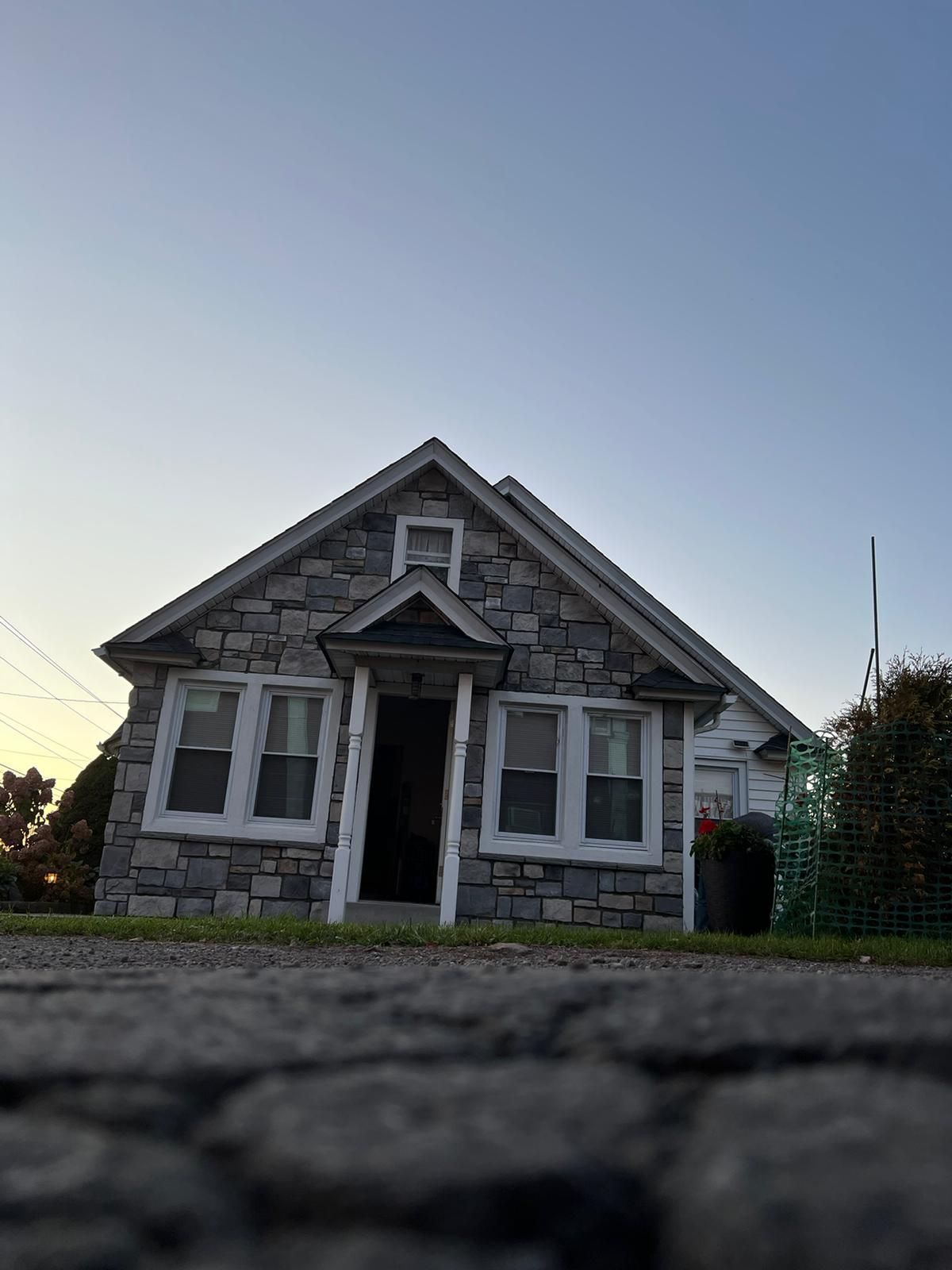 Small gray house with white trim and steep roof, viewed from ground level at sunset.