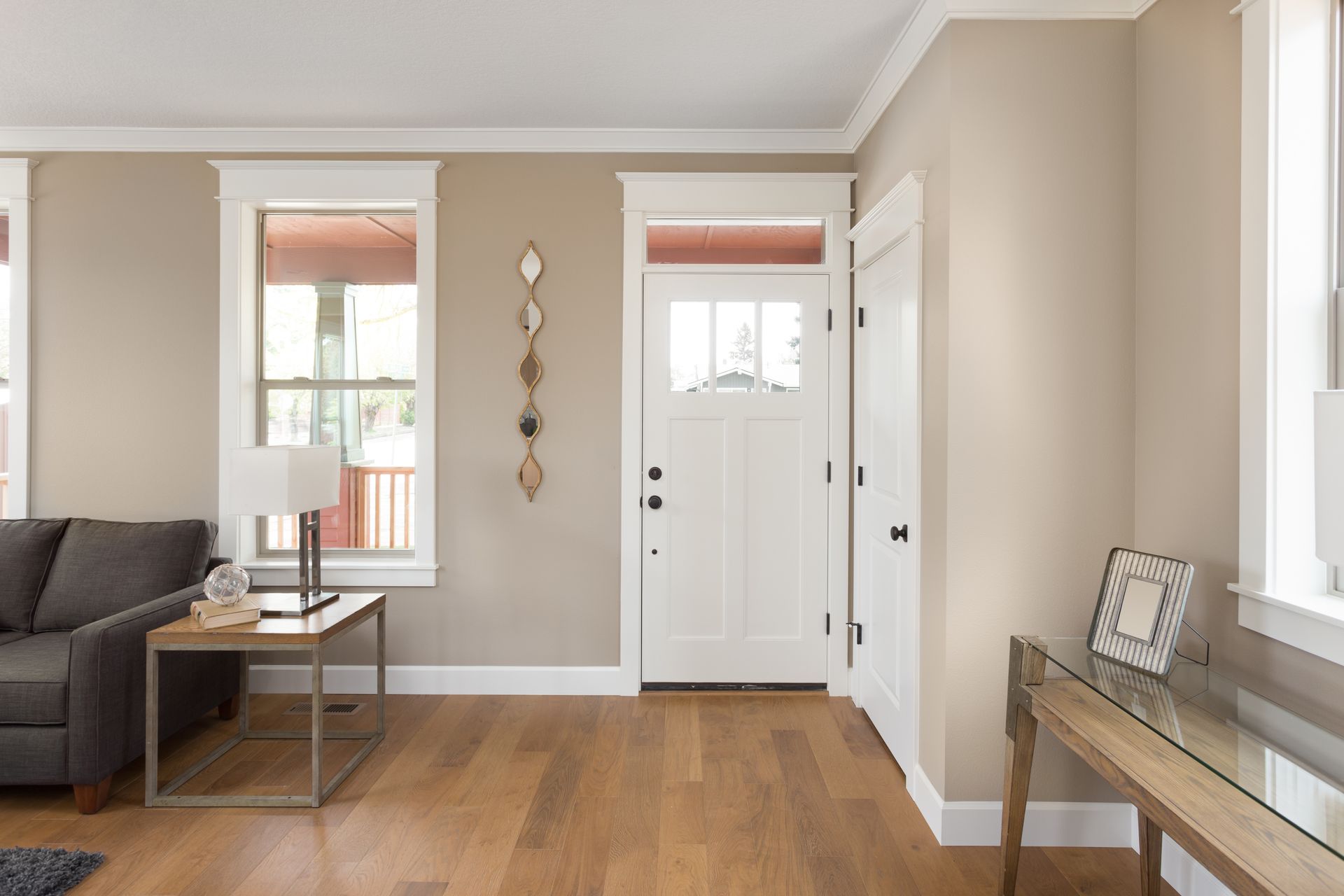 Bright living room with white front door, hardwood floor, gray sofa, and console table by the wall