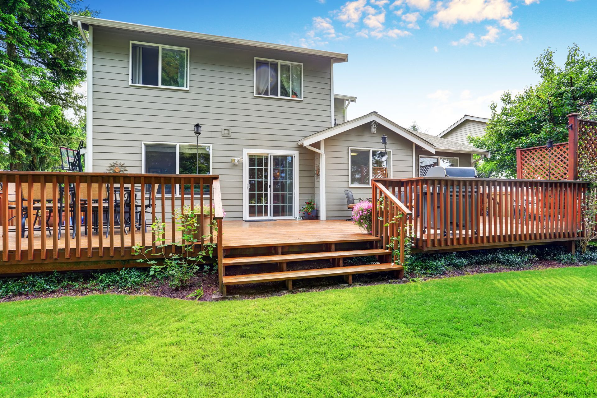 Backyard deck with wooden railings, steps, and a gray two-story house