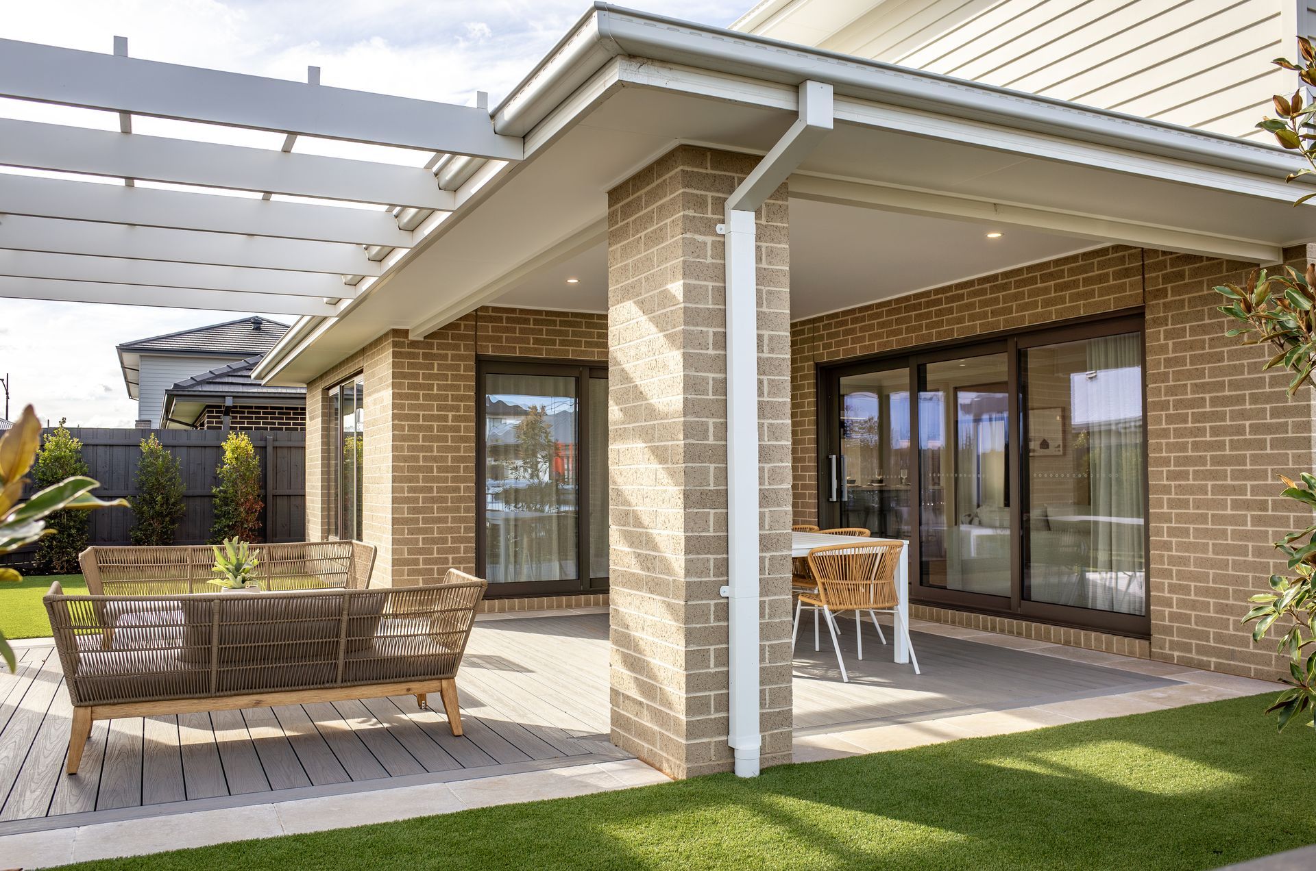 Modern brick patio with outdoor seating, pergola, and sliding glass doors beside a green lawn
