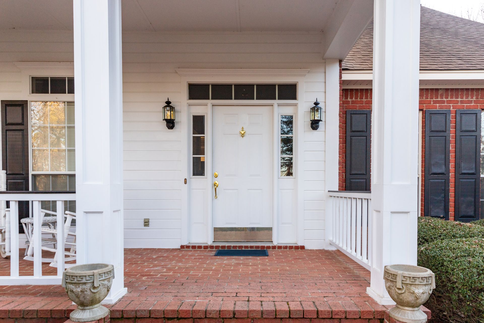 Front porch with white columns, brick floor, and a white front door with sidelights and lanterns