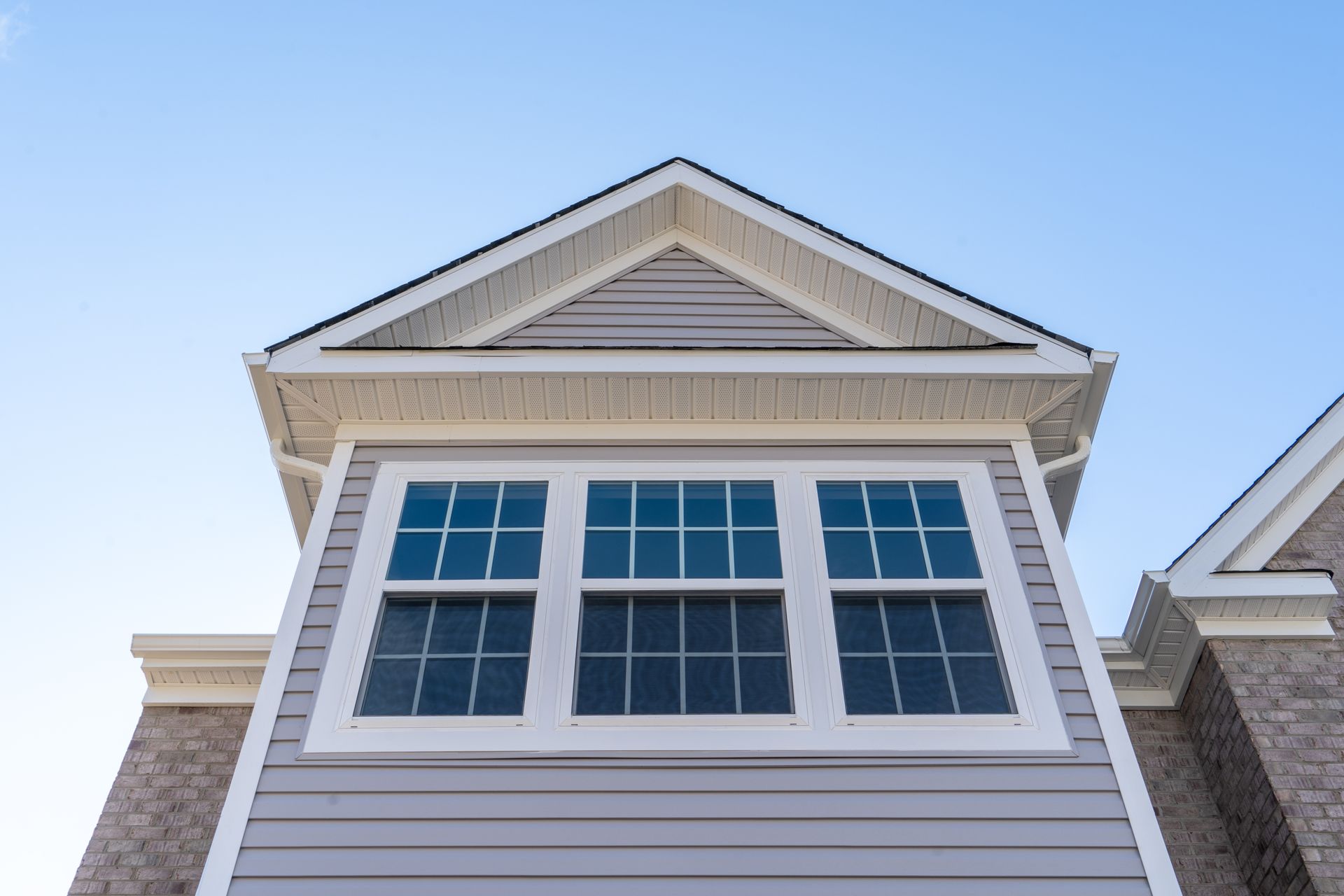 Exterior of a house with white siding, a triangular roof peak, and large windows under a blue sky