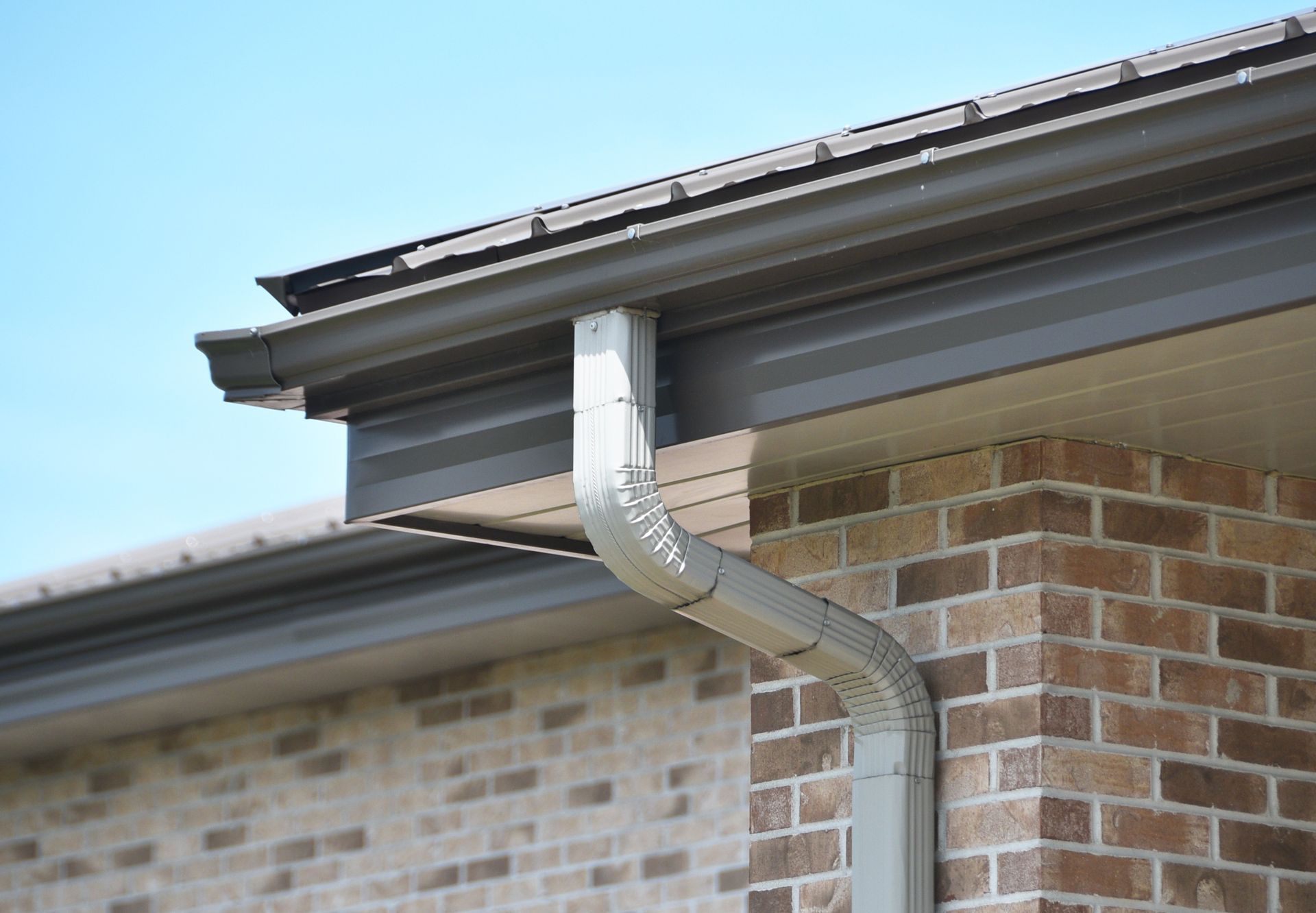 Rain gutter and downspout on the corner of a brick house roof against a blue sky