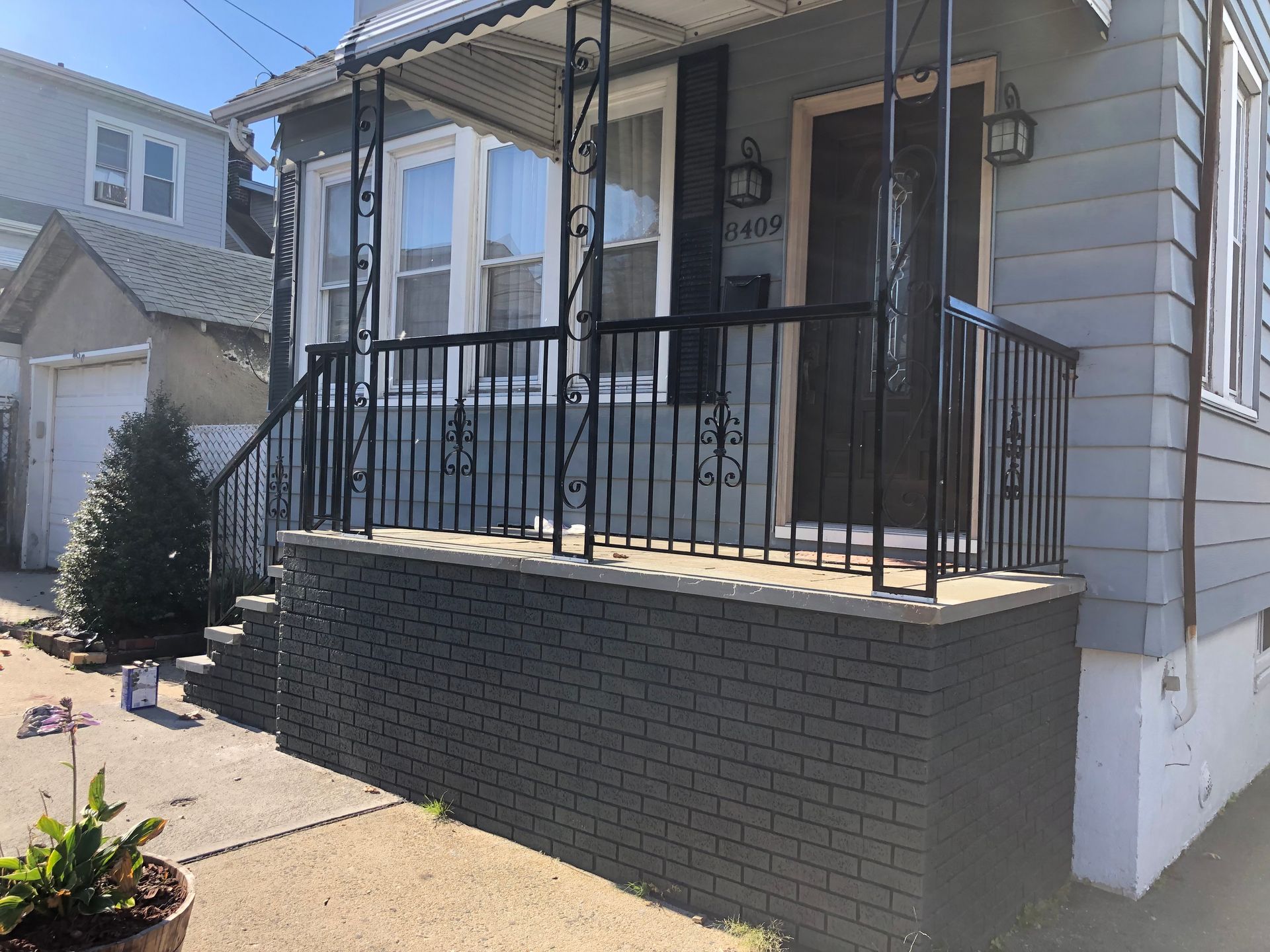 Small front porch with black railings on a gray house beside a concrete driveway.