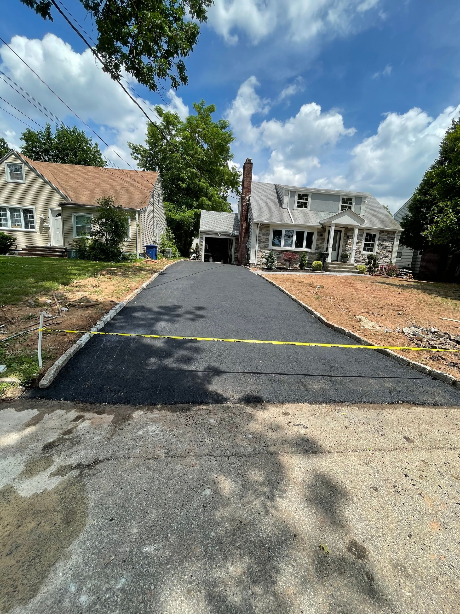 Freshly paved black driveway between two houses, with a yellow caution tape across the entrance. Freshly paved black driveway between two houses, with a yellow caution tape across the entrance.