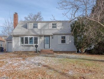 Gray two-story house with a brick chimney, front porch, and snowy yard in winter