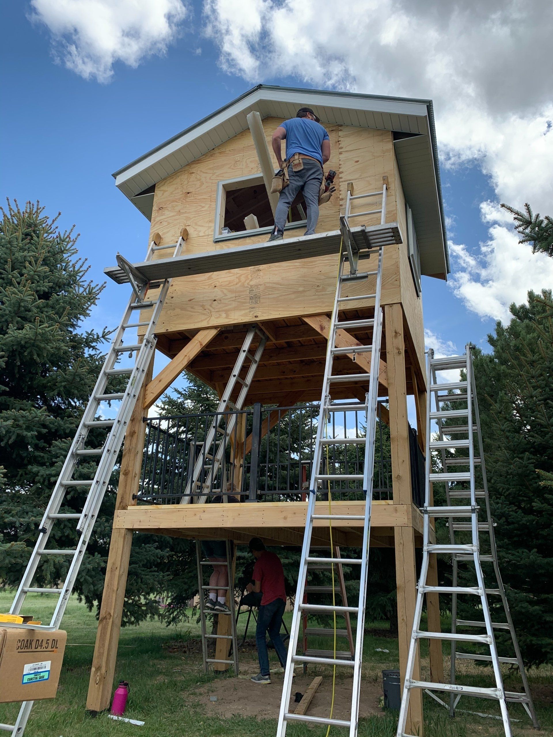 Worker on ladders at a small house under construction on stilts outdoors