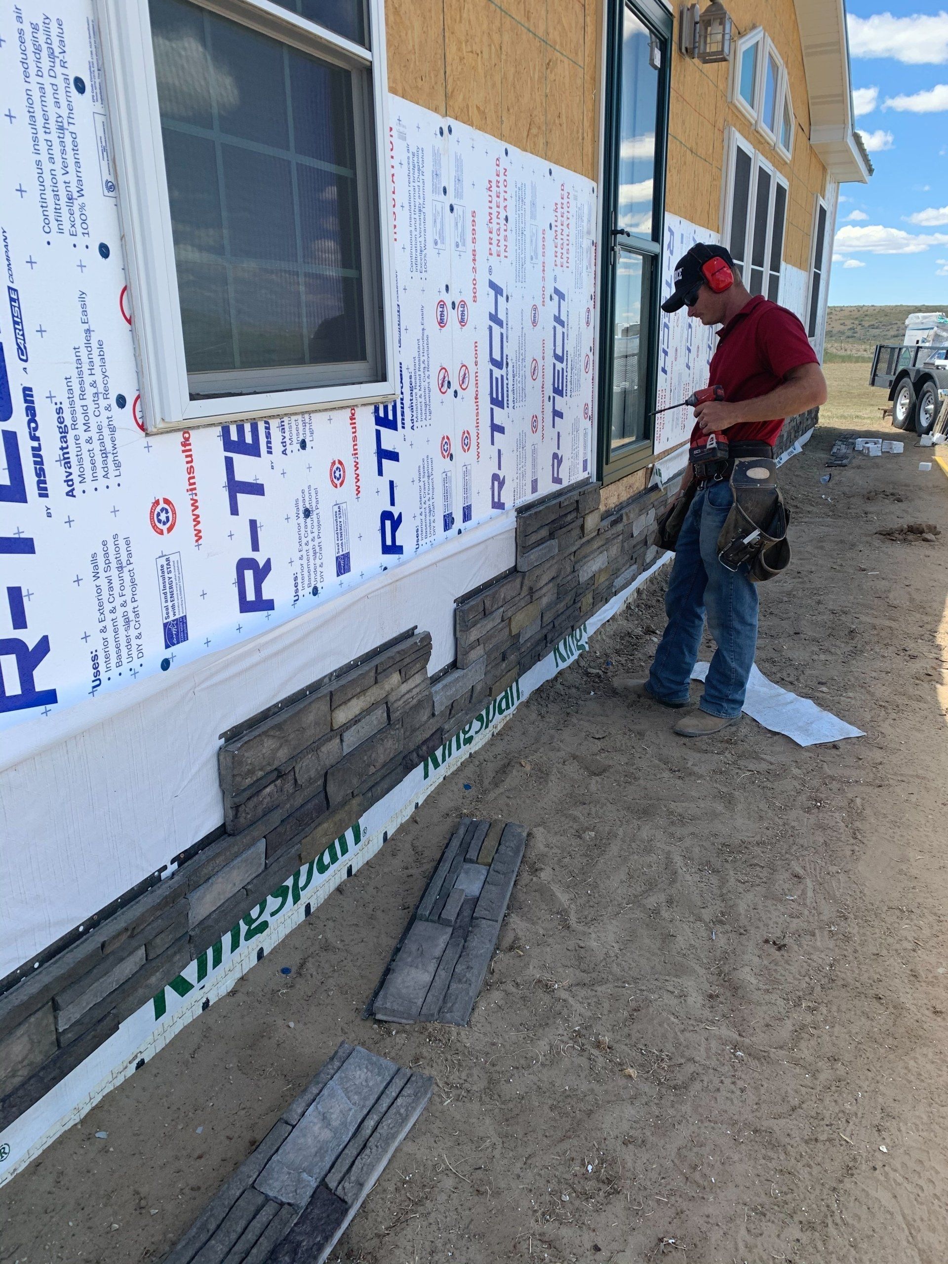 Worker installing exterior foam insulation on a house wall during construction.