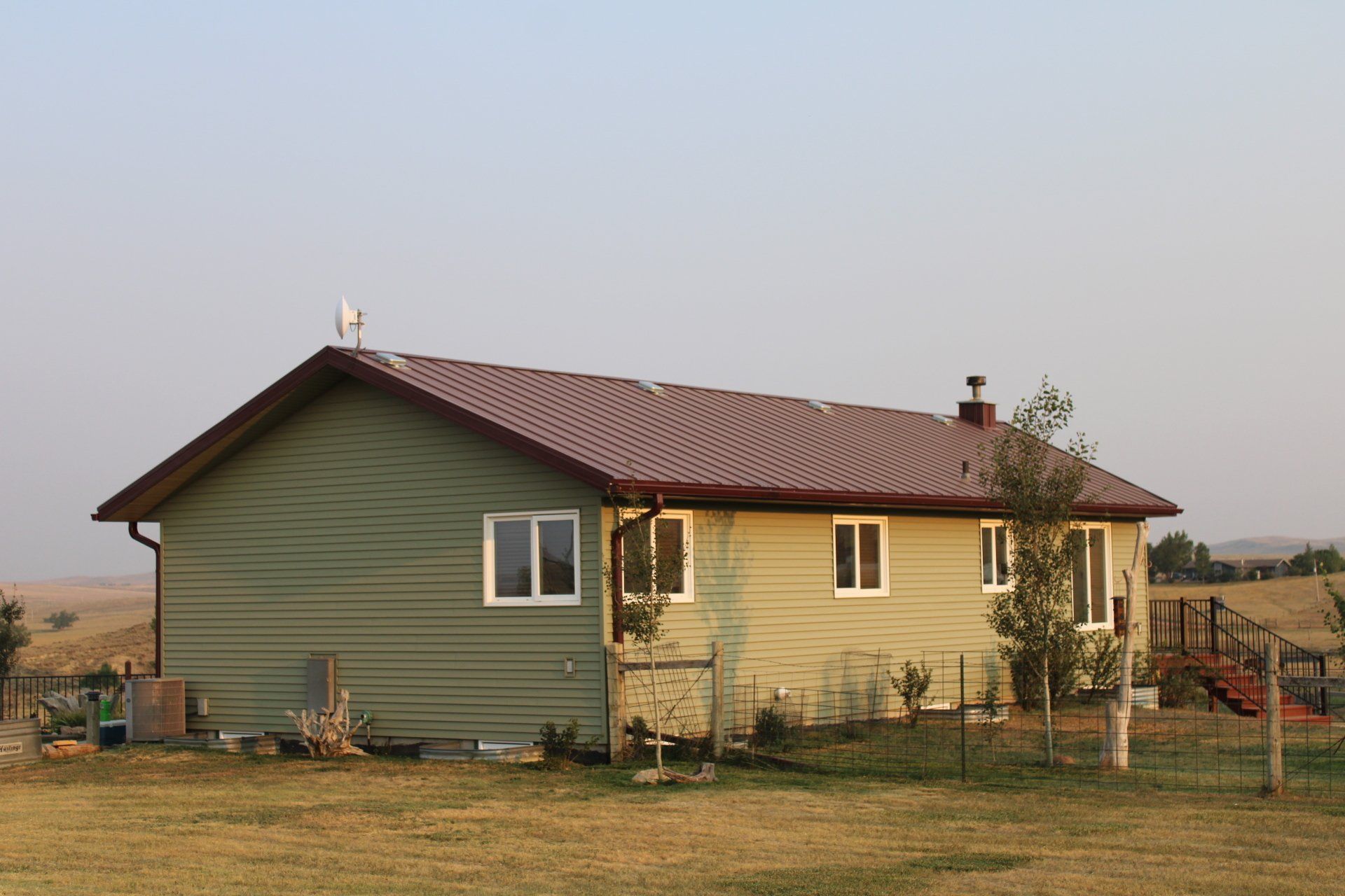 Small single-story house with green siding and a red roof in a rural field at sunset