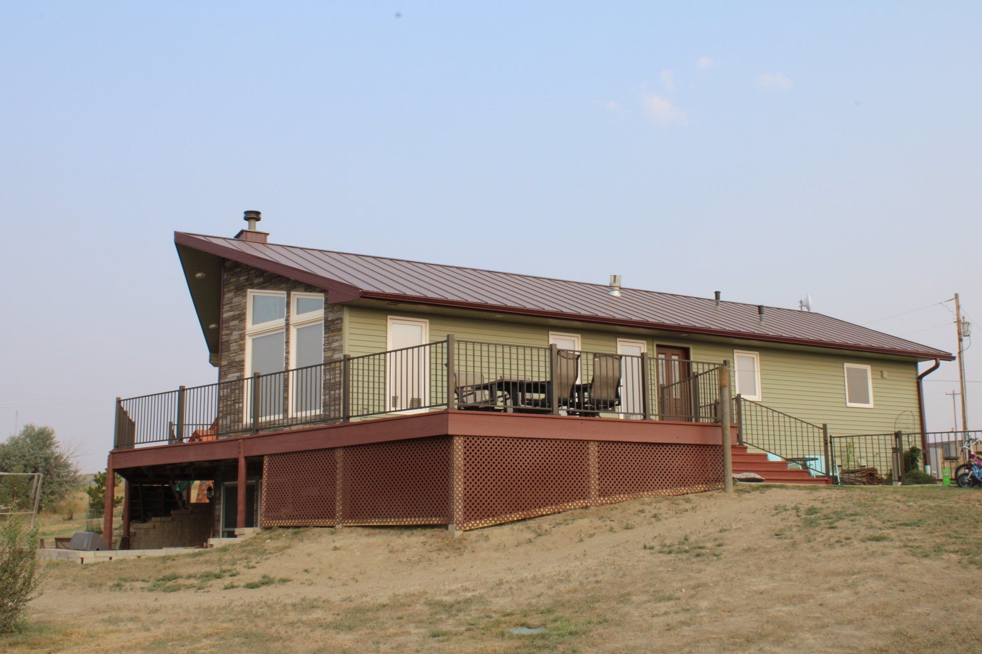 Modern house with sloped roof, wood deck, and large windows on a grassy hillside