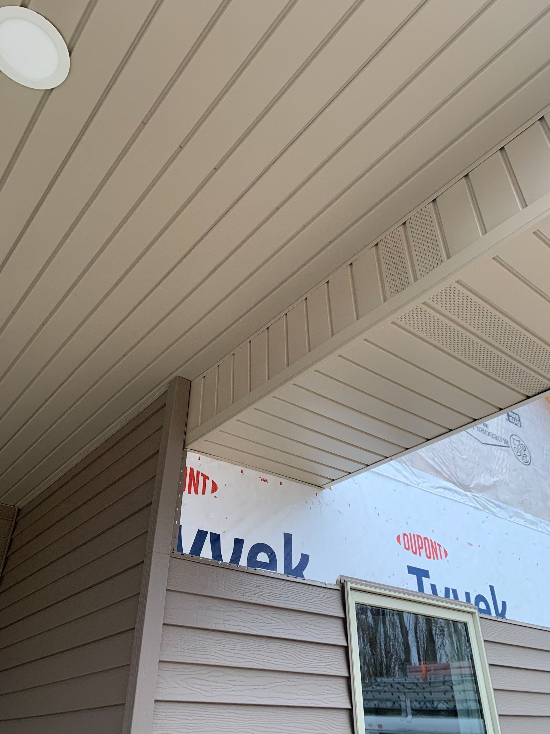 Covered porch with white siding and ceiling, viewed at an angle, with a window and reflected storefront sign.