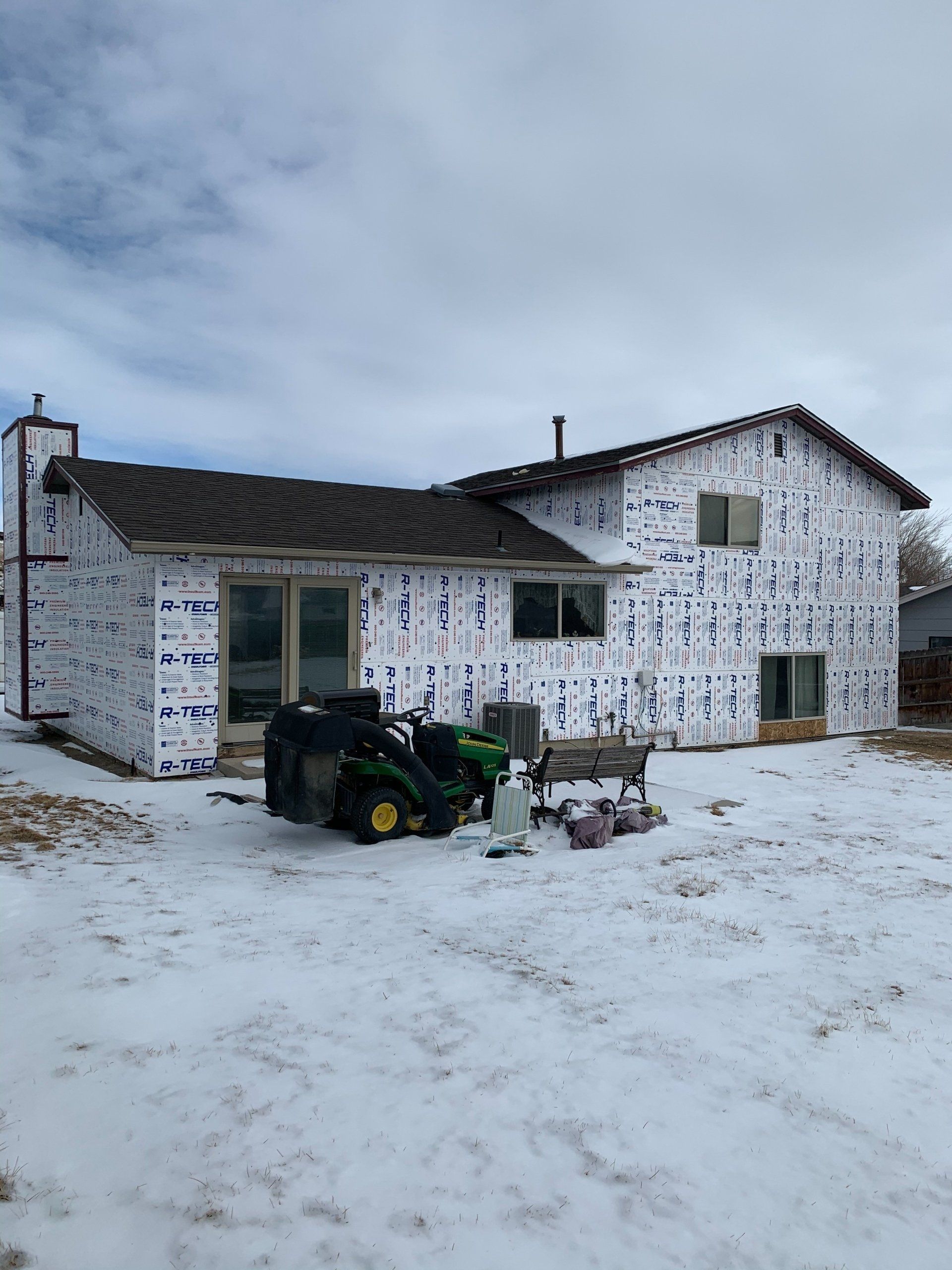 Snow-covered farmhouse with white walls and a parked ATV in the yard under a cloudy sky