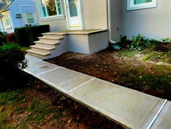 Front steps and a concrete wheelchair ramp beside a beige house with a small garden.