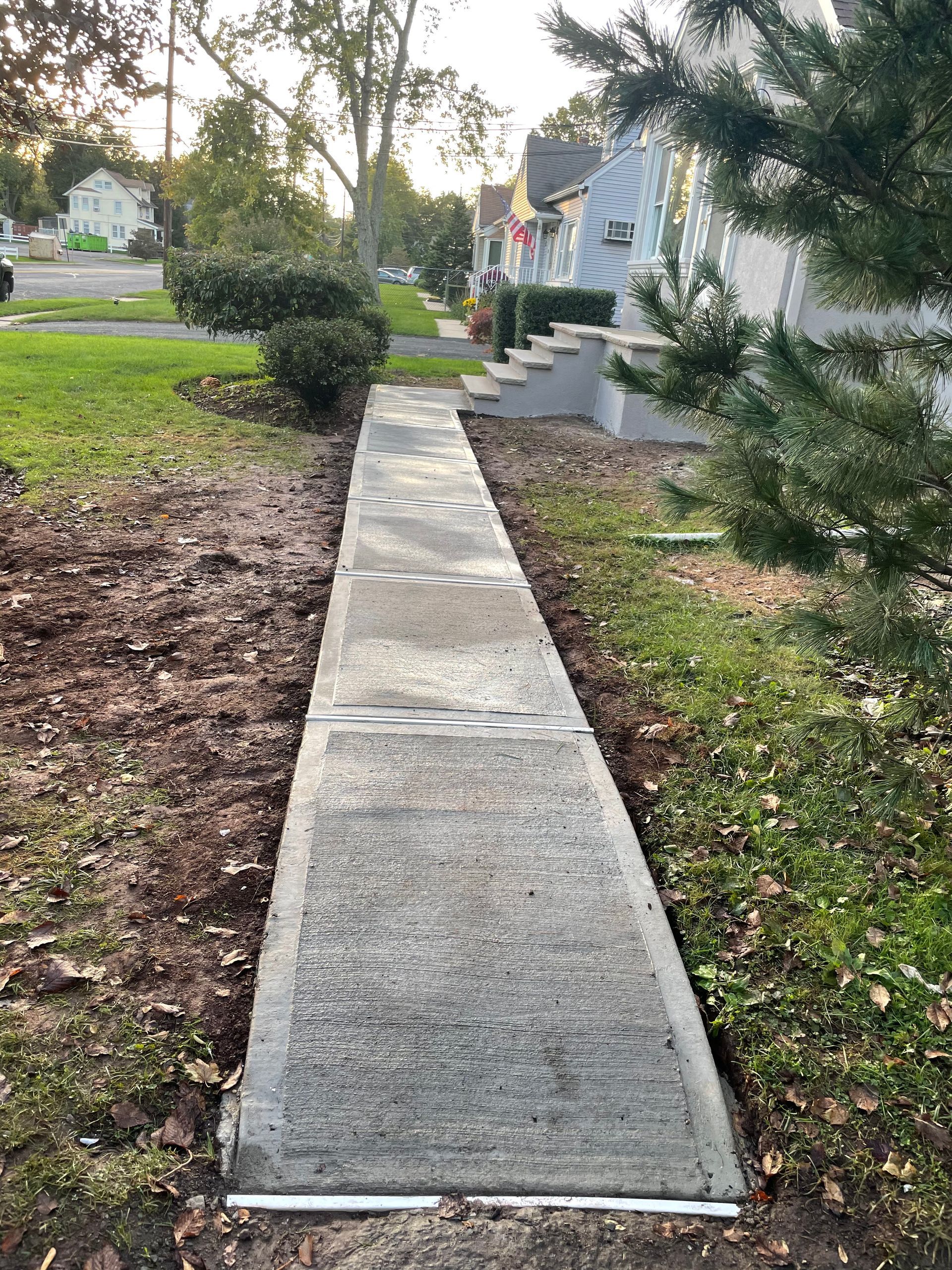Concrete sidewalk path leading through a front yard toward a white house at dusk Concrete sidewalk path leading through a front yard toward a white house at dusk