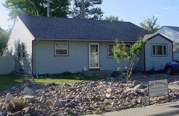 Single-story gray house with blue roof and rock landscaping in front yard