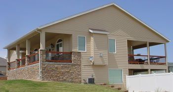 Two-story beige house with stone foundation and covered porch on a grassy lot