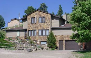 Stone house with brown garage doors and trees on a sunny hillside
