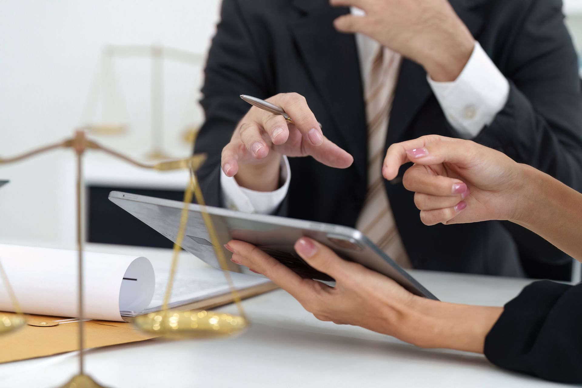 Two people in business attire reviewing documents on a tablet and discussing them. Scales of justice in the background.