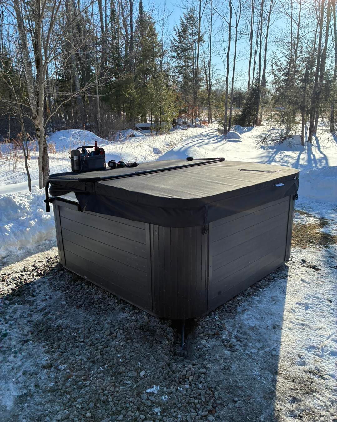 Black outdoor hot tub on snowy ground in a wooded backyard