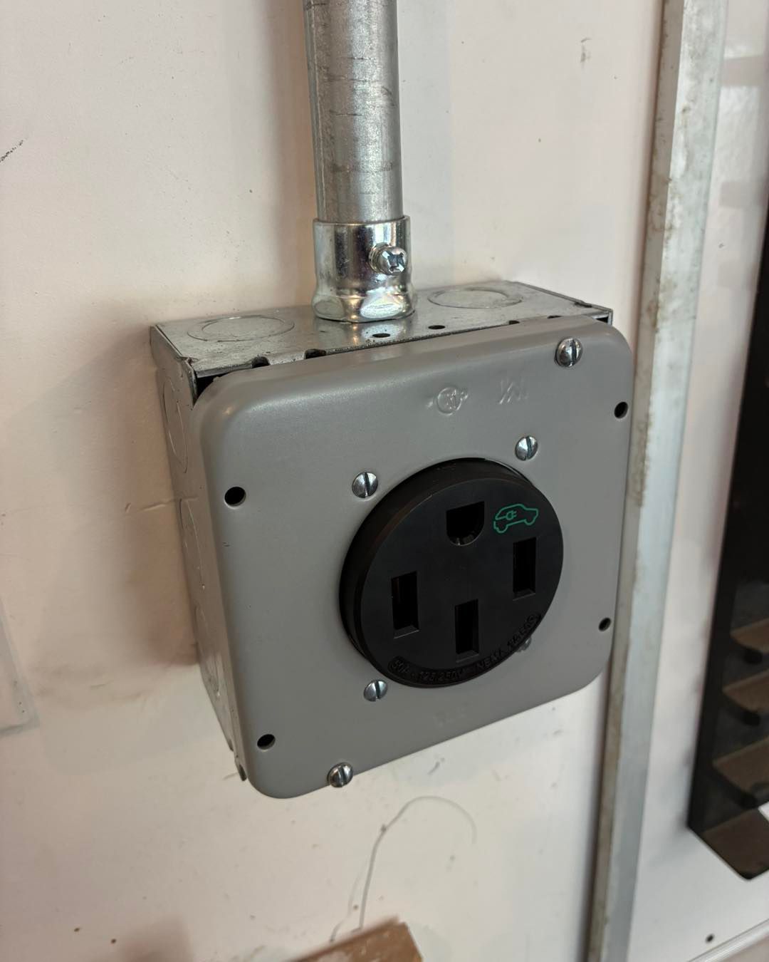 Metal wall electrical outlet box with a black receptacle and conduit attached.
