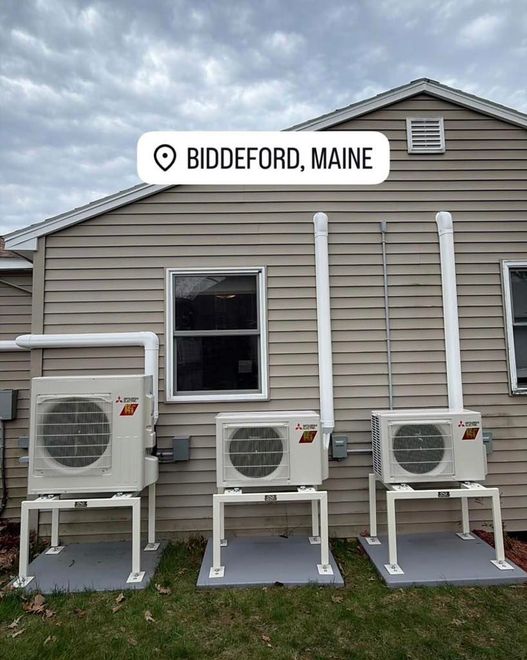 Three outdoor HVAC units on stands beside a beige building in Biddeford, Maine.