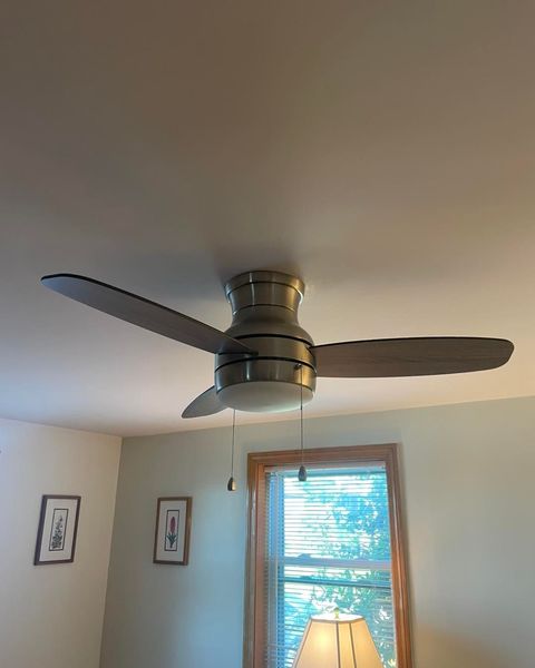 Ceiling fan with dark blades above a window in a light-colored room