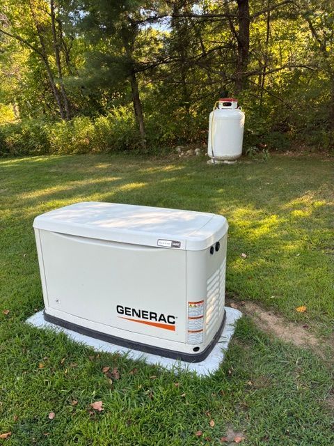 White Generac generator on a concrete pad in a grassy yard, with trees and a propane tank in the background