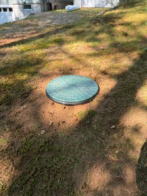 Round green utility cover in a grassy yard with dappled tree shadows.