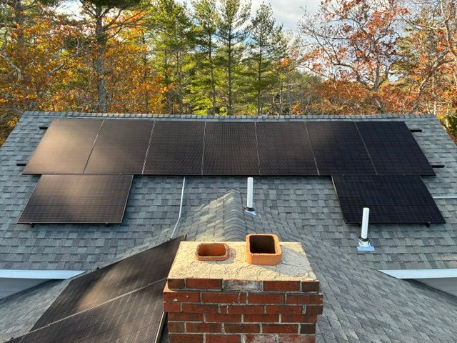 Rooftop solar panels installed beside a brick chimney under autumn trees