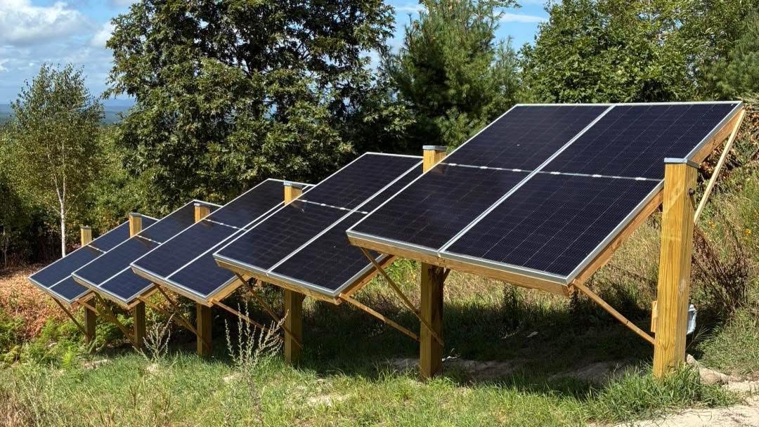 Solar panels mounted on wooden frames in a grassy field under a blue sky