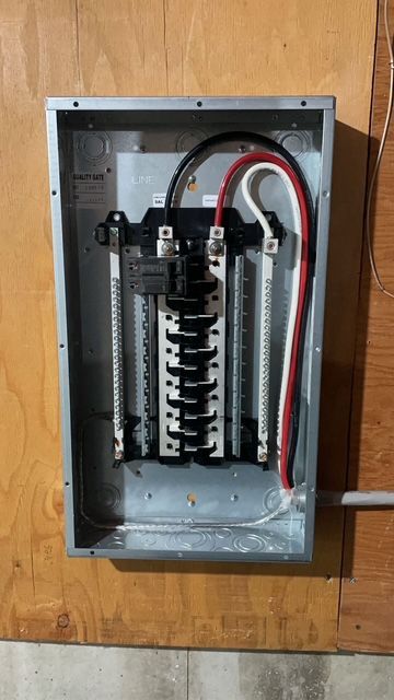 Open electrical breaker panel with circuit breakers and red, black, and white wires mounted on a wooden wall