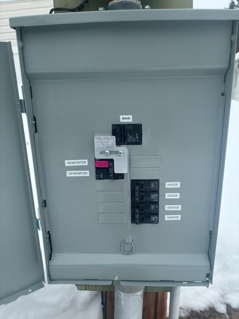 Open electrical panel with circuit breakers and switches on a gray metal enclosure.
