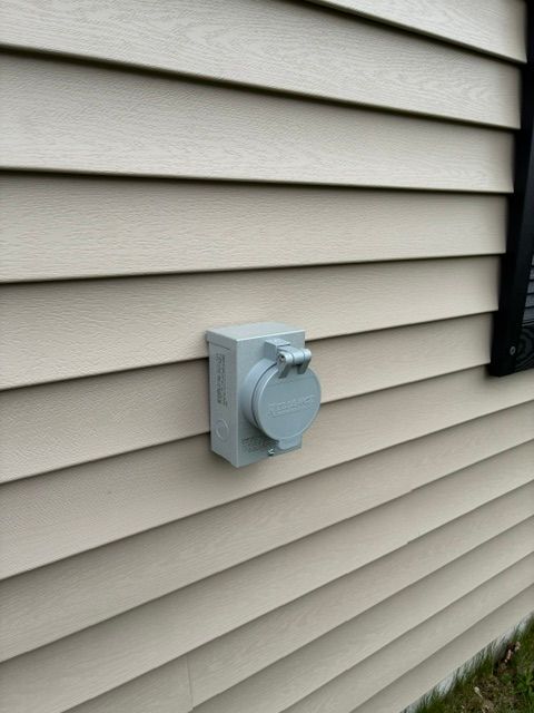 Gray outdoor electrical outlet on beige house siding.