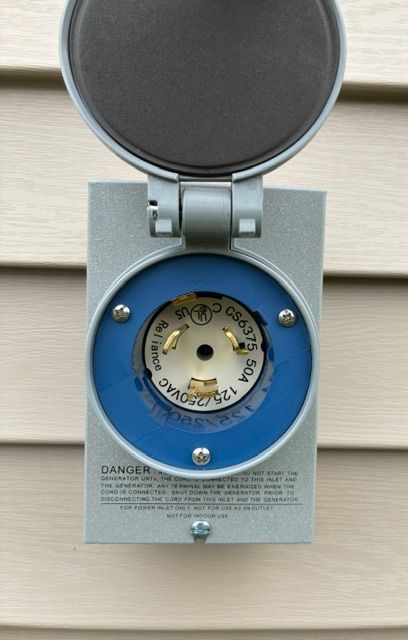 Open outdoor electrical outlet with blue cover on gray box mounted on siding