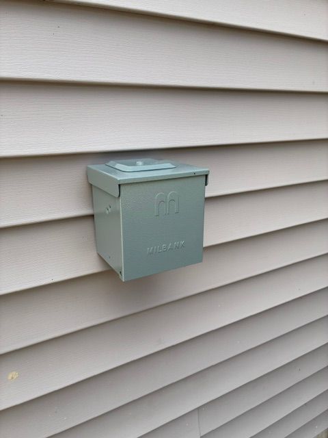 Light green utility box mounted on beige house siding